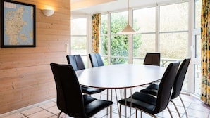 Un coin repas avec une table ronde, des chaises noires, une carte accrochée au mur et de grandes fenêtres avec des rideaux.