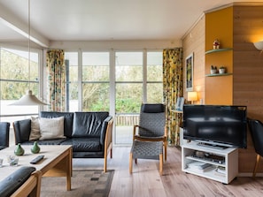 Ein modernes Wohnzimmer mit Sofa, Sessel, TV-Möbel und großen Fenstern.