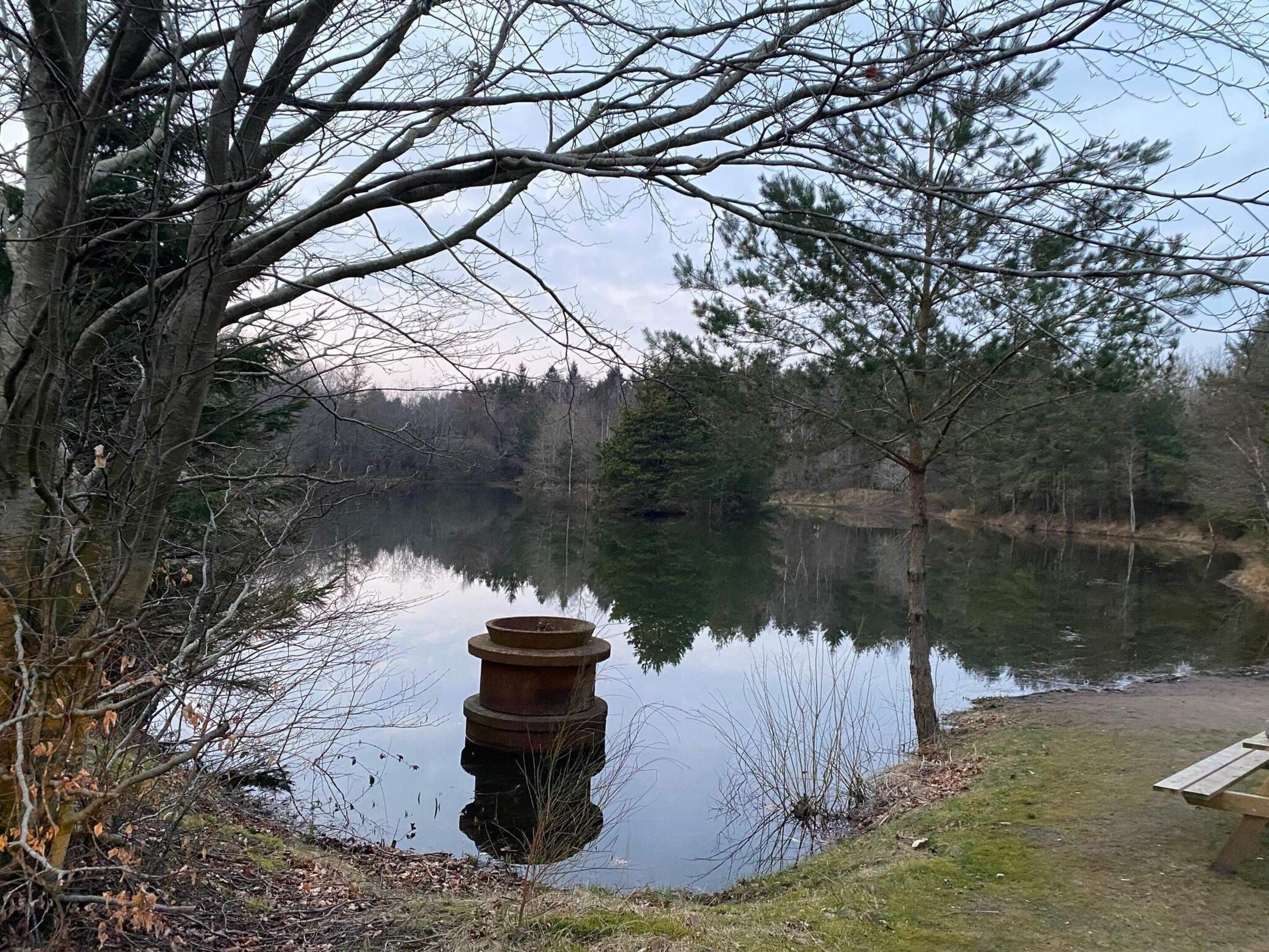Un lac paisible, avec une jetée en bois et une structure métallique dans l’eau.