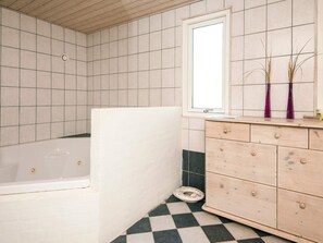 A bathroom with a bathtub, a wooden vanity with drawers, a mirror, and a window. - 4 Star Holiday Home in Oksbol (Oksbol)