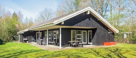A modern house with a covered patio, large windows, and a lawn.