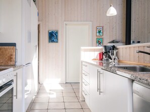 Et moderne køkken med hvide skabe, en granitbordplade, indbygget ovn, kaffemaskine og vask.