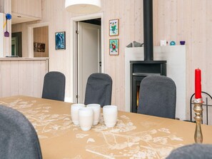 A dining area with a table set for four, a fireplace, and a hallway with wooden walls. - 8 Person Holiday Home in Oksbol (Oksbol)