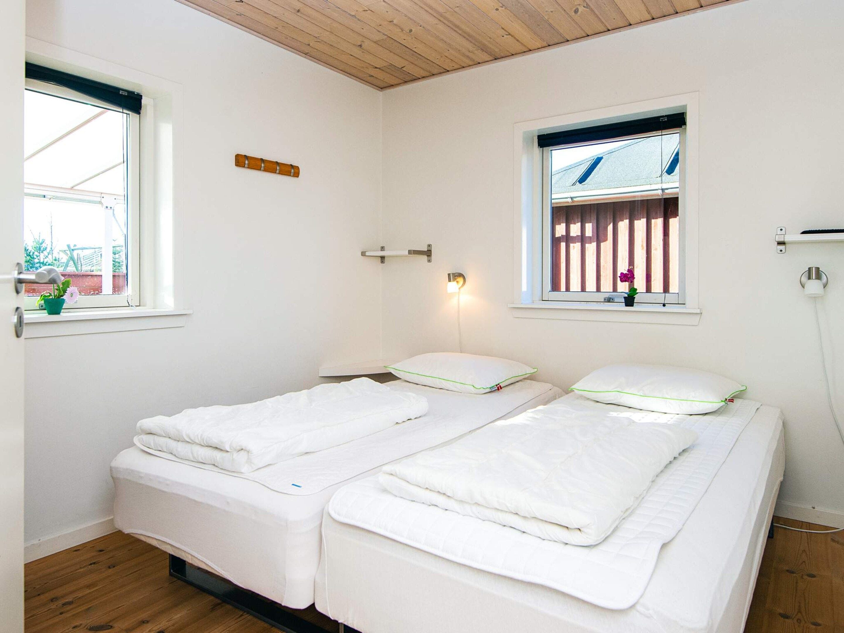 Une chambre avec deux lits, une fenêtre donnant sur une clôture en bois et un luminaire fixé au mur.