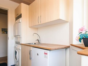 A compact kitchen with a washing machine, a small refrigerator, and wooden cabinets. - 4 Star Holiday Home in Tarm (Tarm)