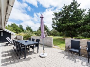 An outdoor patio with a table and chairs, a swing set, and a wooden deck. - 4 Star Holiday Home in Blavand (Blavand)