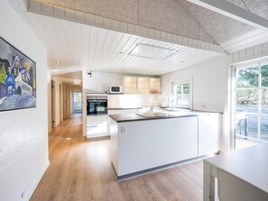 A modern kitchen with a central island, built-in appliances, and a large window providing natural light. - 4 Star Holiday Home in Blavand (Blavand)