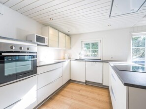 Een moderne keuken met witte kastjes, een inbouwoven en een raam met uitzicht op groen.