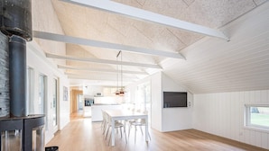 A spacious living area with a large wooden floor, a central island dining table, and a modern fireplace. - 4 Star Holiday Home in Blavand (Blavand)