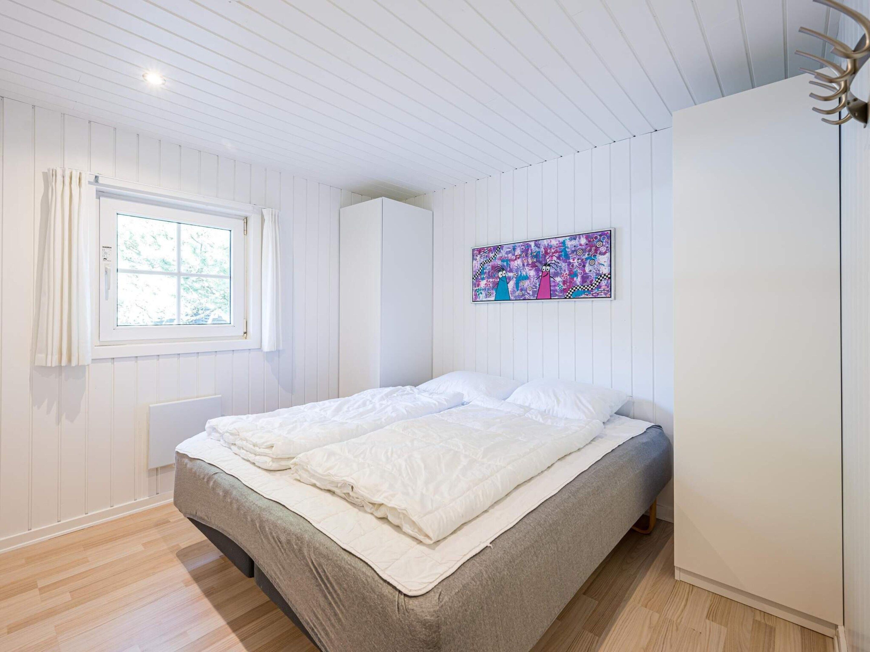A bedroom with a bed, a window with curtains, a wall-mounted artwork, and a wardrobe.