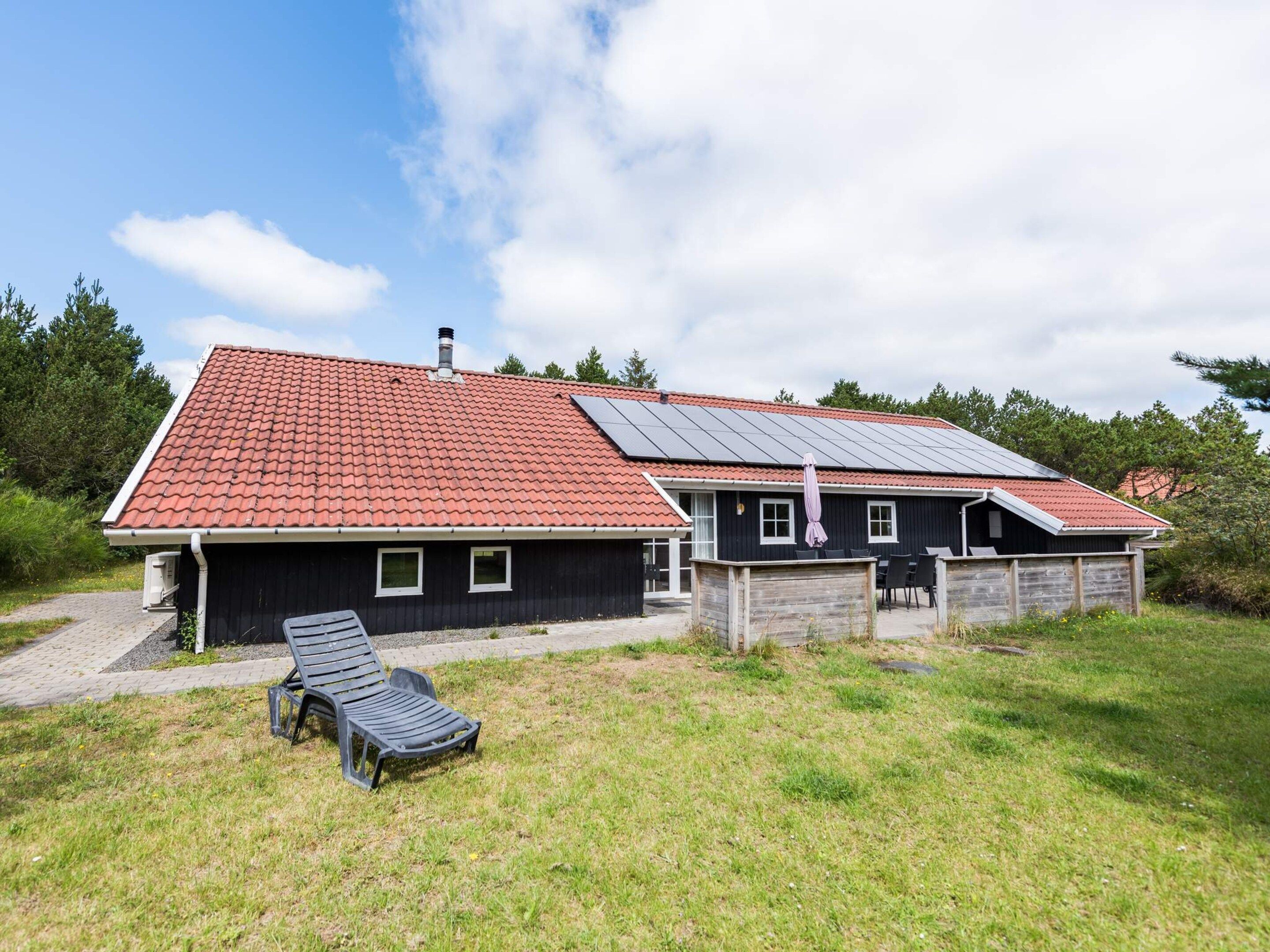 A two-story house with a red-tiled roof, a covered patio area, and a grassy yard.