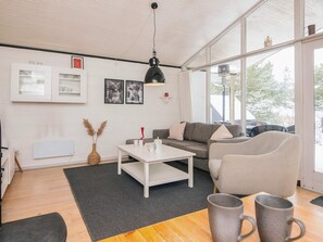 Ein modernes Wohnzimmer mit einer Couch, Sesseln, einem Couchtisch und einem großen Fenster mit Blick ins Freie.