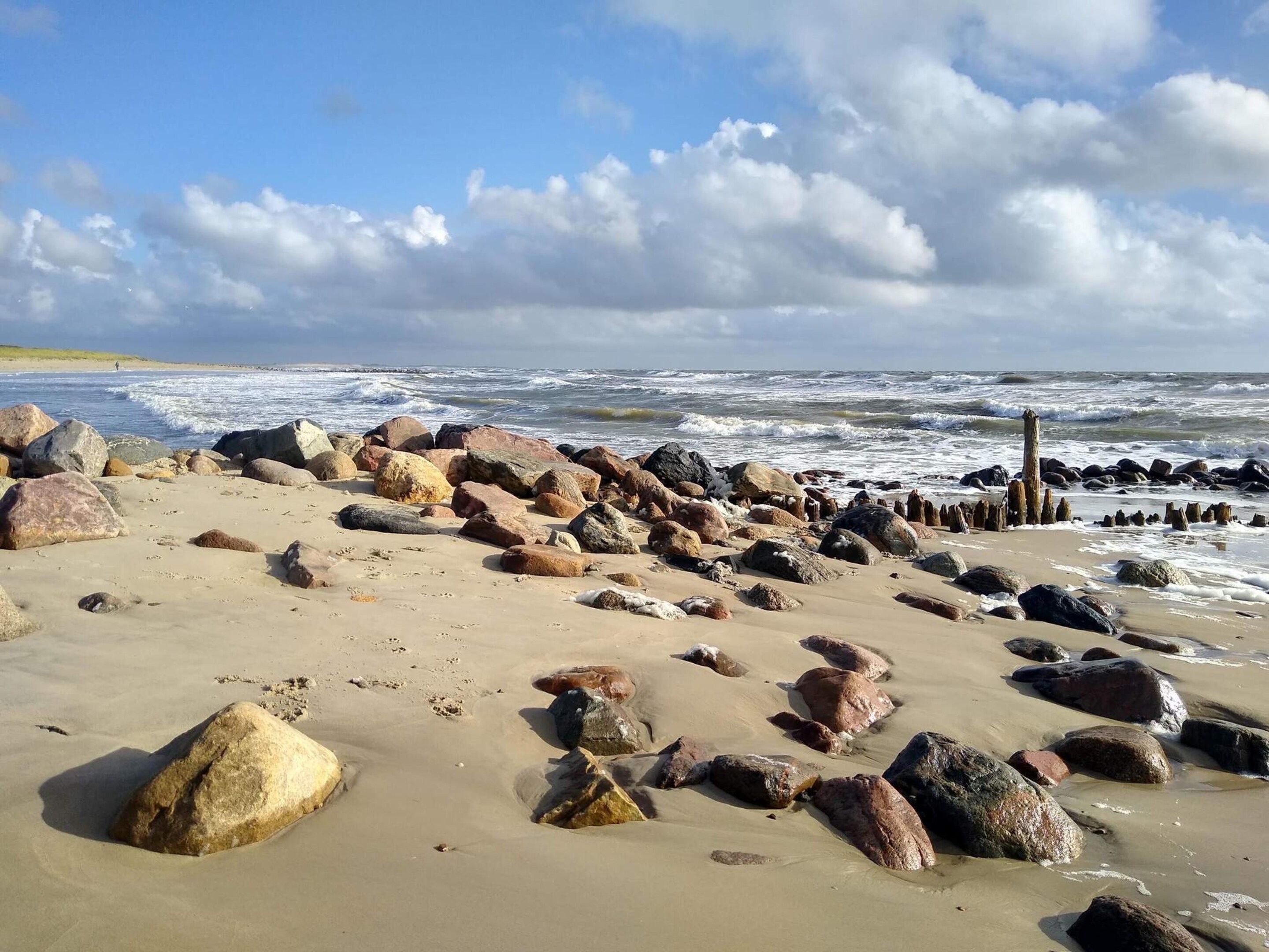 Een strand met grote rotsen en een houten constructie in het water.