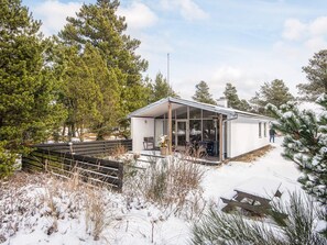 A modern cabin with a glass enclosure, surrounded by snow-covered ground and pine trees. - 4 Person Holiday Home in Blavand (Blavand)