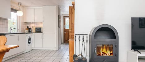 A modern kitchen with a built-in washing machine, a wooden dining table, and a wood-burning stove.