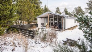 A modern house with a glass-enclosed patio, surrounded by snow-covered ground and pine trees.