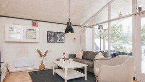 A modern living room with a sofa, armchairs, a coffee table, and a large window offering a view of the outdoors.