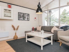 A modern living room with a white sofa, a coffee table, and a large window with a view of trees.