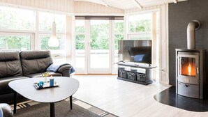 A modern living room with a sofa, coffee table, TV, and a wood-burning stove. - 5 Star Holiday Home in Hemmet (Hemmet)
