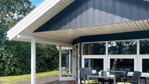 A covered patio with a table and chairs, large windows, and a view of the surrounding greenery. - 5 Star Holiday Home in Hemmet (Hemmet)