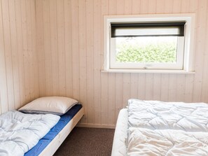 A room with two single beds, a window with a view of greenery, and wooden walls.