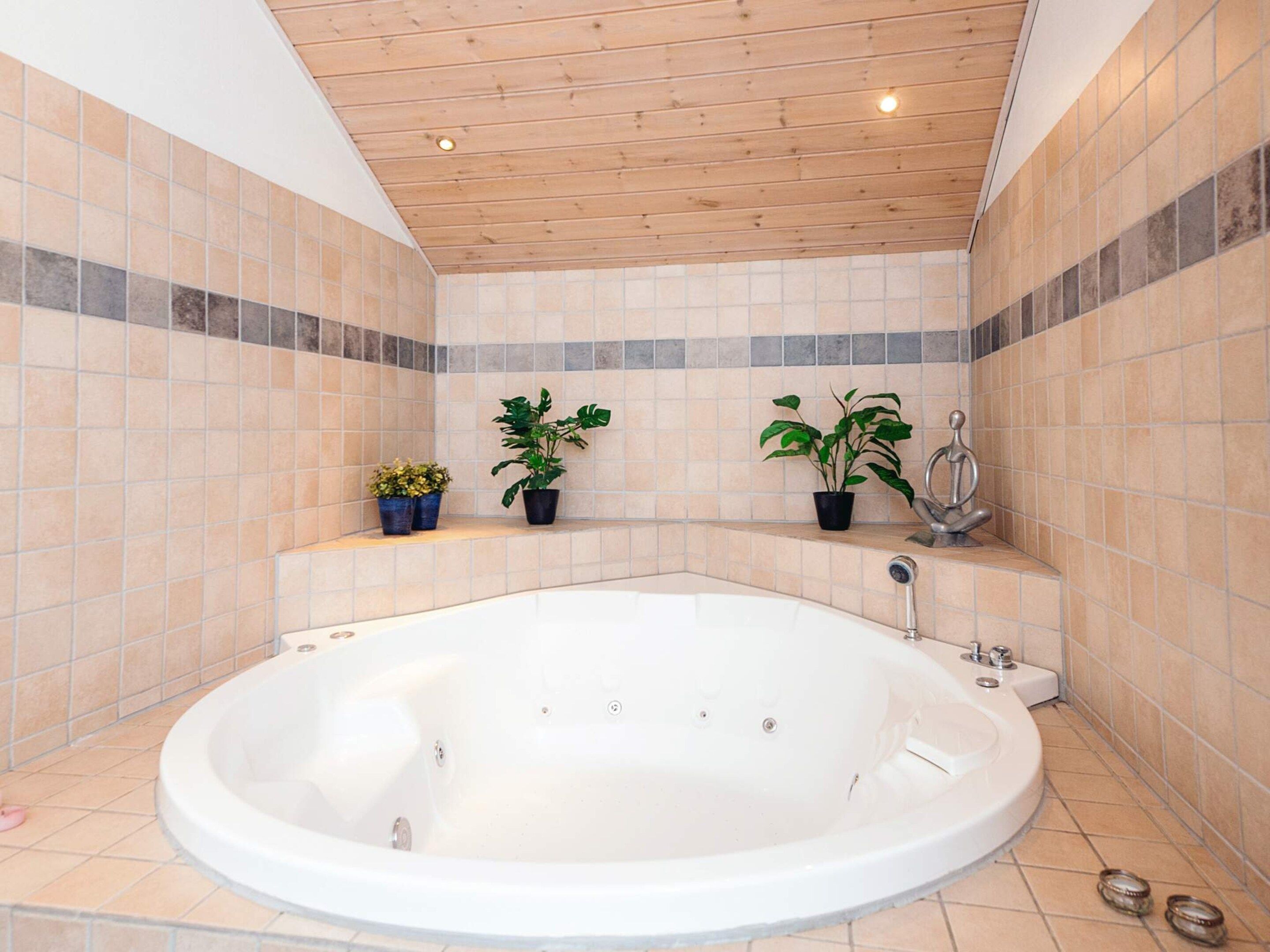 Un baño con una bañera independiente, paredes de azulejos y techo de madera.