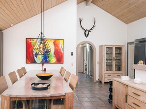Un comedor con una mesa grande, sillas, una lámpara colgante, un cuadro abstracto de colores y una cabeza de ciervo montada.