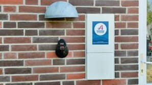 Un muro de ladrillo con un letrero azul y una caja blanca, posiblemente un medidor o panel de control.