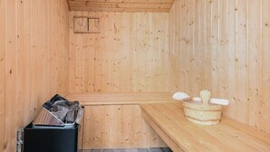 Un sauna con paredes de madera, un banco, un cubo de basura y un balde de madera con asa.