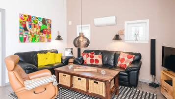 A living room with a sofa, armchair, coffee table, and a colorful abstract painting.