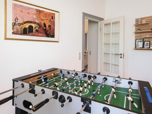 Une pièce avec une table de baby-foot, un tableau encadré au mur et une porte donnant sur une autre pièce.