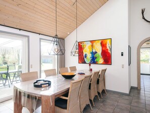 Un espace repas moderne avec une grande table, des chaises en osier et un tableau abstrait aux couleurs vives accroché au mur.
