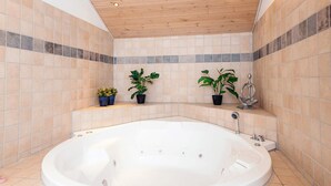 Un baño con una bañera grande, paredes con azulejos y techo de madera.