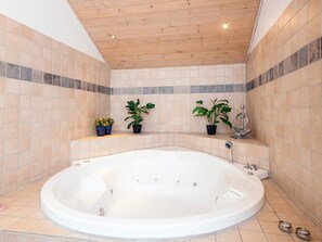 A bathroom with a large bathtub, tiled walls, and wooden ceiling. - 5 Star Holiday Home in Norre Nebel (Norre Nebel)
