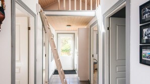 A hallway with a wooden staircase leading to a loft, white doors, and a black and white photo on the wall. - 5 Star Holiday Home in Norre Nebel (Norre Nebel)