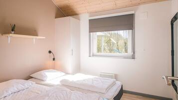Une chambre avec deux lits, une fenêtre donnant sur un terrain de jeux, une étagère avec une plante et un plafond en bois.