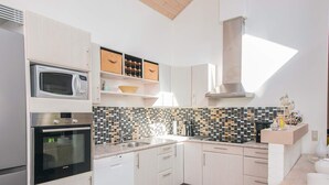 A modern kitchen with white cabinets, a microwave, an oven, a tiled backsplash, and a wooden ceiling. - 5 Star Holiday Home in Norre Nebel (Norre Nebel)