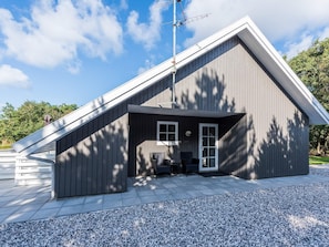 A modern building with a sloped roof, a small porch with seating, and a satellite dish. - 8 Person Holiday Home on a Holiday Park in Blåvand (Blavand)