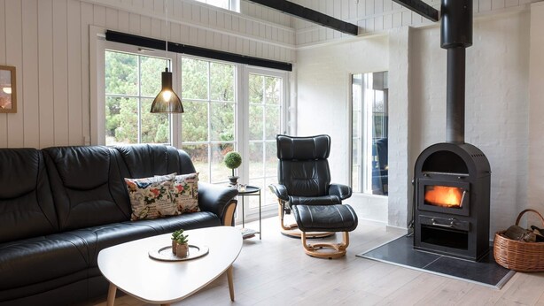 Un salon moderne avec un canapé en cuir noir, une table basse blanche, un fauteuil en cuir noir et une cheminée avec une hotte noire.