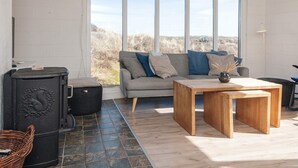 Ein Wohnzimmer mit Sofa, Tisch, Kamin und Blick durch große Fenster.