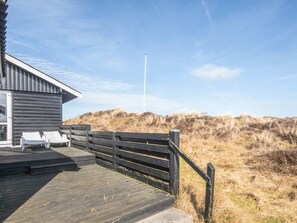 A wooden deck with two lounge chairs, a building with a dark exterior, and a grassy dune landscape in the background. - 4 Person Holiday Home in Fano (Fano)