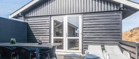 Une cabane en rondins avec une terrasse, une table et des chaises, ainsi que deux chaises longues.