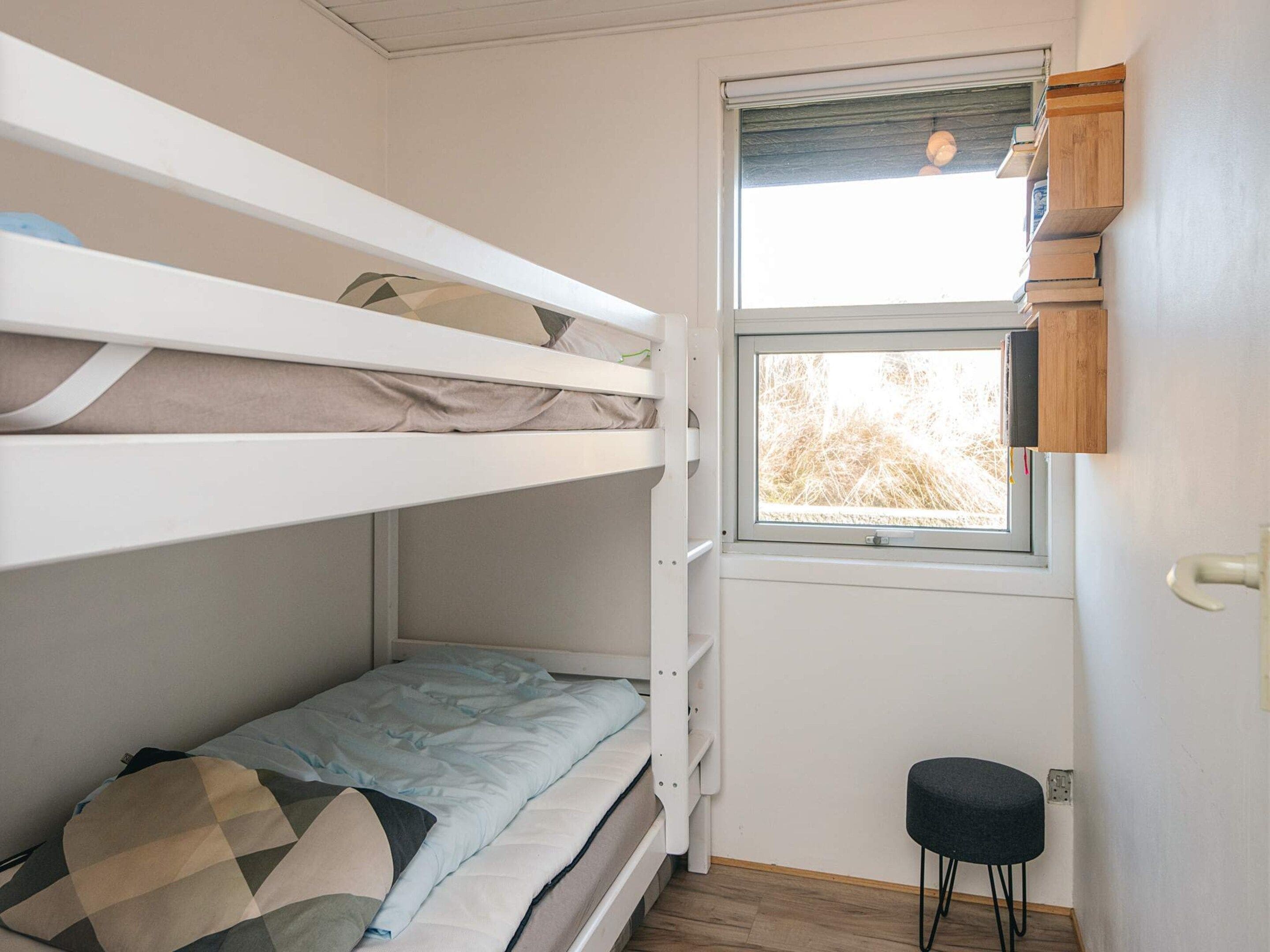 Een slaapkamer met een stapelbed, een raam en een klein krukje.