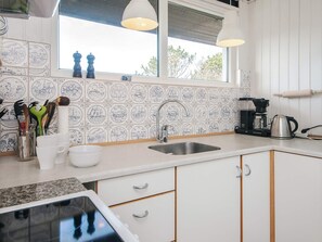 A kitchen with white cabinets, a stainless steel sink, and a window with a view of trees. - 4 Person Holiday Home in Fano (Fano)