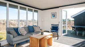 Ein modernes Wohnzimmer mit Sofa, Couchtisch und Sessel, großen Fenstern und Blick ins Freie.
