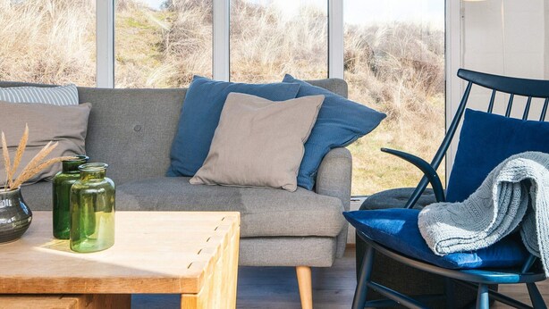Ein gemütliches Zimmer mit einem grauen Sofa, einem blauen Sessel und einem Holztisch mit grünen Glasbehältern.