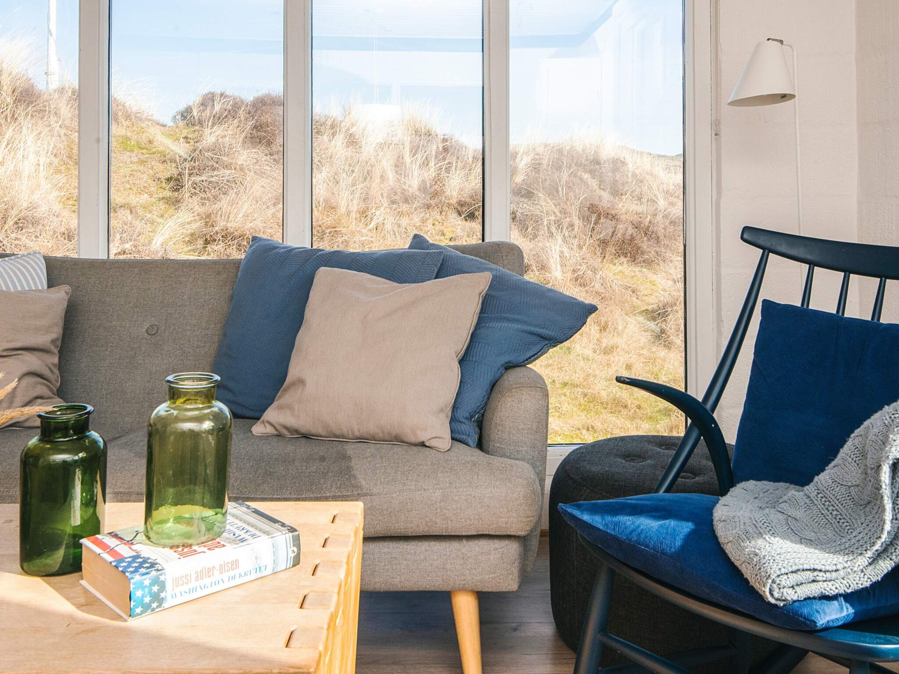 A room with a grey sofa, a blue chair, and a table with books and glass bottles.