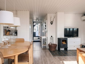 Een moderne keuken met een open haard, een eethoek met een houten tafel en stoelen, en een televisie aan de muur.