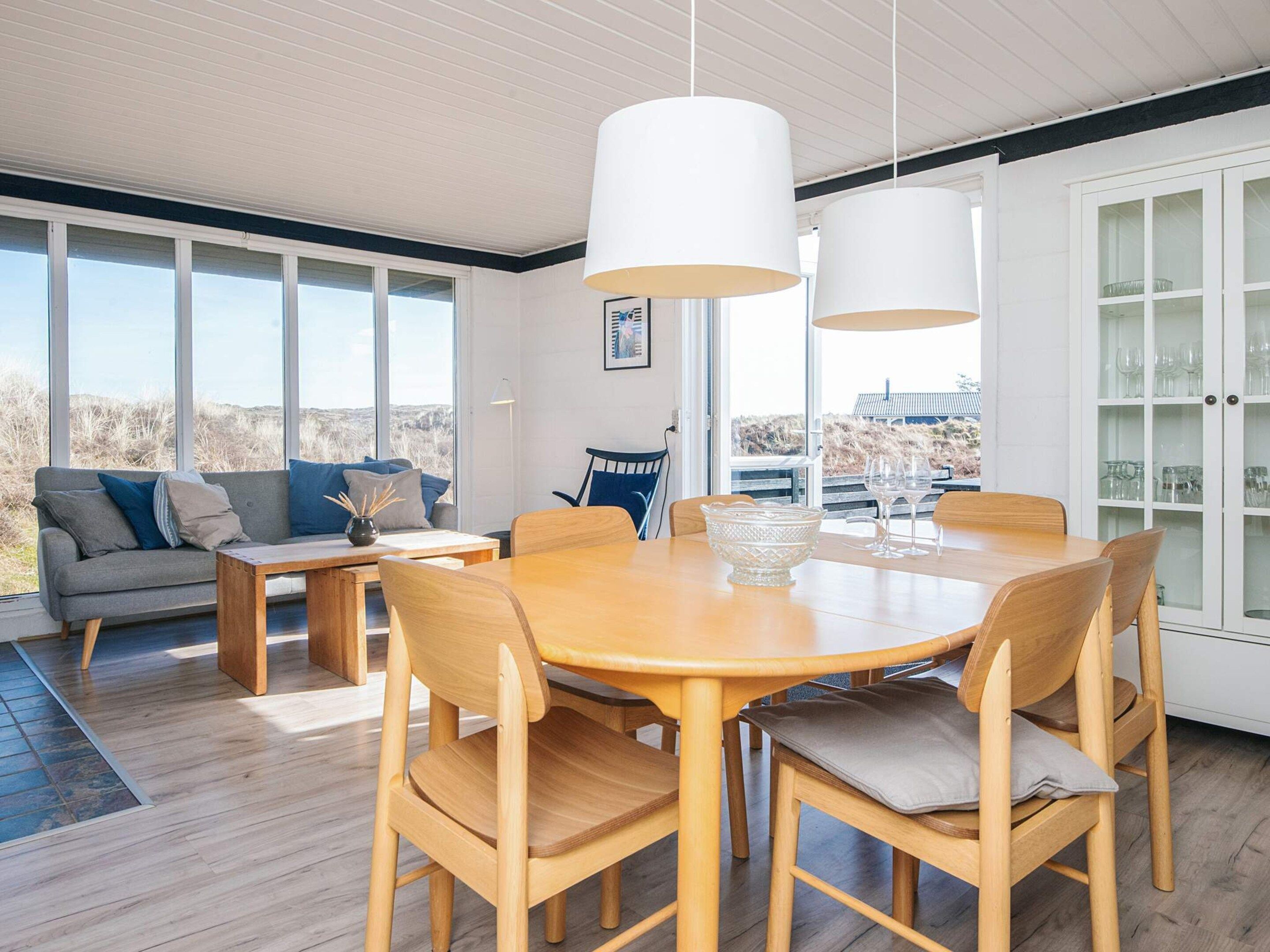 Uma sala de jantar moderna com mesa e cadeiras de madeira, janelas amplas e vista para o exterior.