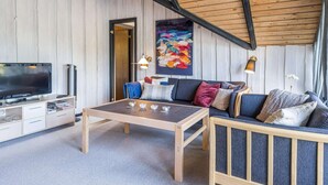 Un soggiorno accogliente con soffitto in legno, una TV a schermo piatto, un divano con cuscini, un tavolino da caffè e un quadro appeso al muro.